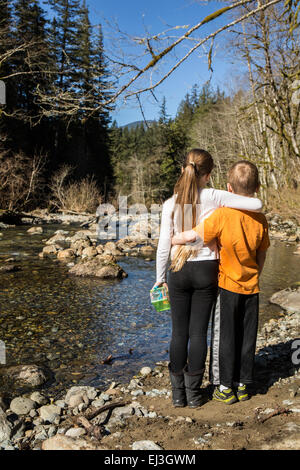 Neunjähriges Mädchen umarmt ihre sieben Jahre alten Bruder, wie sie innehalten und liebevoll, den Blick auf die flachen Snoqualmie River Stockfoto