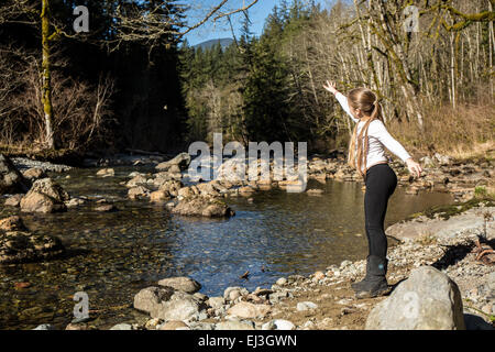 Neunjähriges Mädchen warf einen Stein (mit dem Felsen in der Luft) in Snoqualmie River, in der Nähe von North Bend, Washington, USA Stockfoto