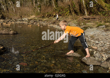 Sieben Jahre alter Junge spielt mit einem Stock in der flachen Snoqualmie River in der Nähe von North Bend, Washington, USA Stockfoto