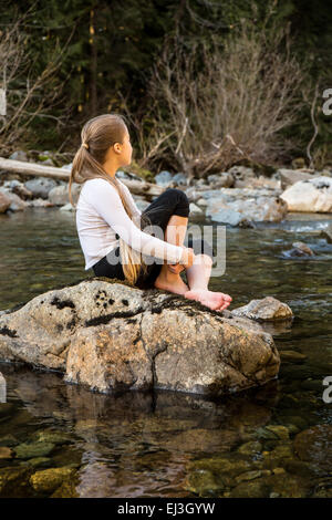 Neunjähriges Mädchen träumen, sitzt auf einem Felsen in der flachen Snoqualmie River in der Nähe von North Bend, Washington, USA Stockfoto