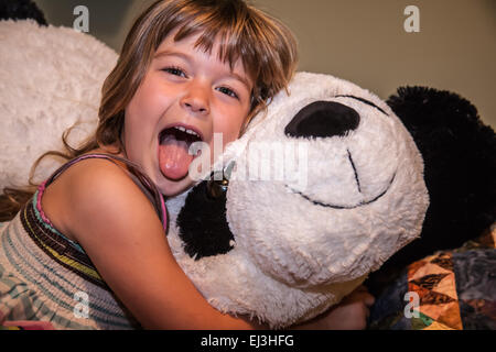 Vier Jahre altes Mädchen handeln, durch ihre Zunge heraus, umarmt ihr große, gefüllte Panda Bär Stockfoto