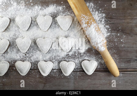 Knödel kochen. Rohe herzförmige Knödel, Mehl und Nudelholz auf hölzernen Hintergrund. Ansicht von oben. Stockfoto