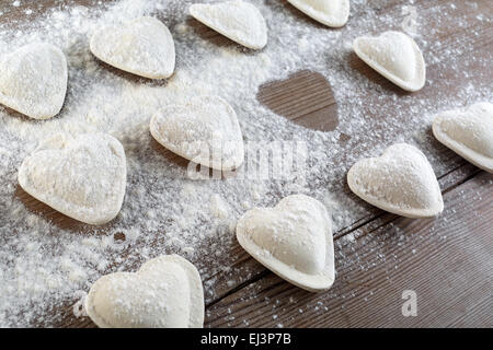 Ravioli kochen. Rohe Klöße in Form von Herzen bestreut Mehl auf hölzernen Hintergrund Closeup. Geringe Schärfentiefe. Stockfoto