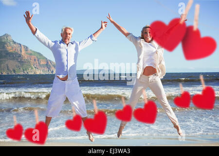 Zusammengesetztes Bild des glücklichen Paares springen am Strand zusammen Stockfoto