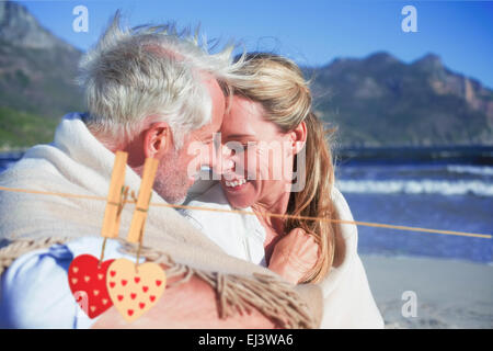 Zusammengesetztes Bild des lächelnden paar sitzt am Strand unter Decke Stockfoto