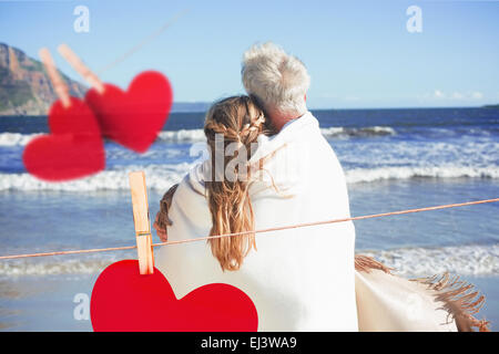 Zusammengesetztes Bild des Paares eingehüllt in Decke am Strand, Blick auf das Meer Stockfoto