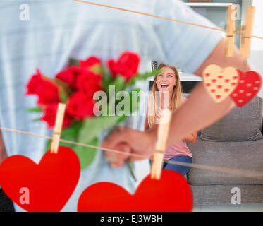 Zusammengesetztes Bild des Mannes versteckt Strauß Rosen von lächelnden Freundin auf der couch Stockfoto