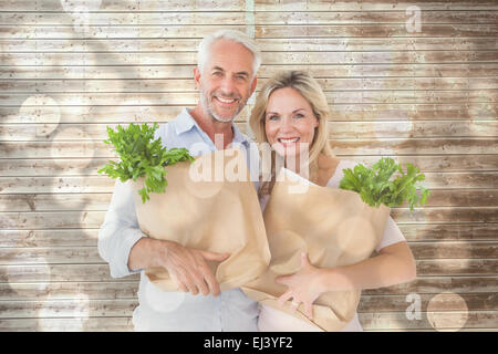 Zusammengesetztes Bild des glücklichen Paares tragen Papier-Einkaufstüten Stockfoto