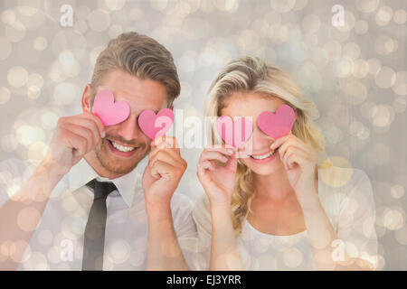 Zusammengesetztes Bild attraktives junges Paar rosa Herzen über Augen halten Stockfoto