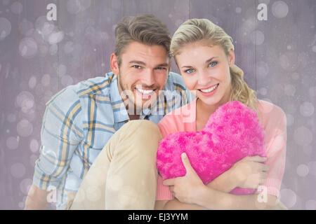 Zusammengesetztes Bild attraktives junges Paar sitzen halten Herz Kissen Stockfoto