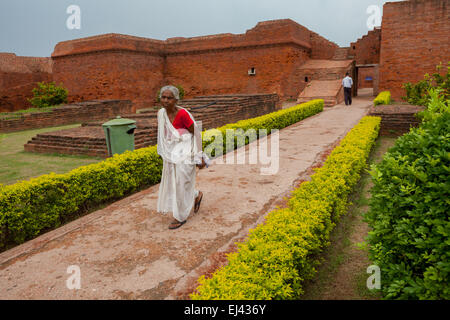 Eine Seniorin wird fotografiert, während sie auf einem Gehweg am alten buddhistischen Universitätskomplex von Nalanda in Nalanda, Bihar, Indien, läuft. Stockfoto