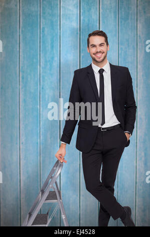 Zusammengesetztes Bild des lächelnden Geschäftsmann stützte sich auf Trittleiter Stockfoto