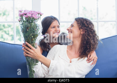 Glückliche Mutter und Tochter sitzen auf der Couch mit Blumen Stockfoto