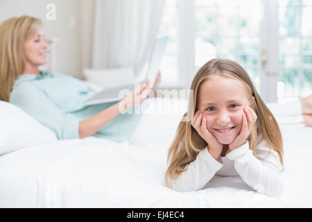 Kleines Mädchen Blick in die Kamera während Mutter mit laptop Stockfoto