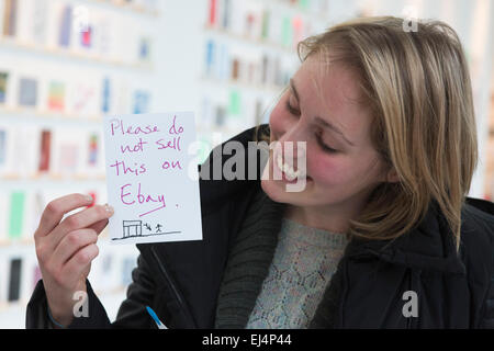 London, UK. 21. März 2015. Im Bild: Jessica Milligan, die ganze Nacht in der Warteschlange hatte, hält das Kunstwerk "Bitte nicht das bei Ebay von Jeremy Deller verkaufen". Viele Kunstliebhaber in der Warteschlange an der Royal College of Art Dyson Builing durch die Nacht, erster in der Linie für den Stewarts Recht RCA Geheimnis Postkarte Vertrieb sein die heute beginnt. RCA-Geheimnis ist eine jährliche Spendenaktion der Postkarte Größe Arworks um Geld für die RCA Fine Art Student Award Fund. In diesem Jahr 3.000 angezeigt Kunstwerke, darunter Arbeiten von berühmten Künstlern wie Bob & Roberta Smith, Paula Rego und Nick Park - die sind anonym - ar Stockfoto