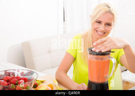 Eine schöne Reife Frau vorbereiten, einen Smoothie oder Saft mit Früchten in der Küche. Stockfoto