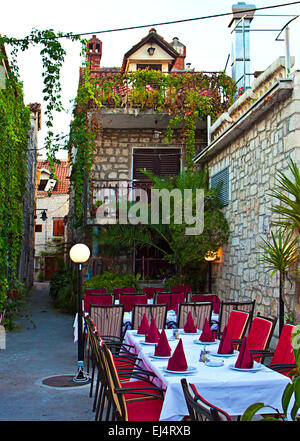 Trogir Kroatien, es ist spät abends, Lampen angezündet und ein Restaurant mit Sitzplätzen und Tischen auf der Straße ist bereit für die Touristen Stockfoto