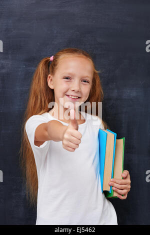 Lächelndes Ingwer Mädchen mit Büchern und Daumen nach oben zeigen Stockfoto
