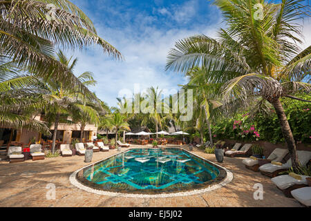 Poolbereich mit Liegestühlen von Palmen in Mia Resort Mui Ne umgeben. Mui Ne, Binh Thuan Provinz, Vietnam. Stockfoto