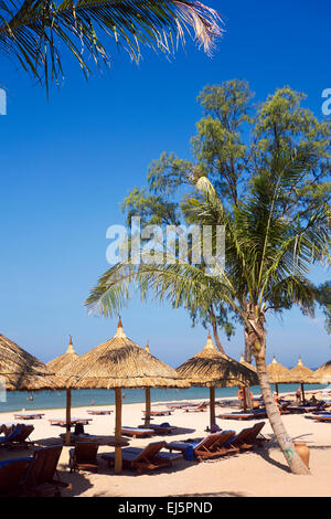 Palme und strohgedeckten Sonnenschirmen und Liegestühlen am Strand von Vinpearl Resort. Insel Phu Quoc, Provinz Kien Giang, Vietnam. Stockfoto