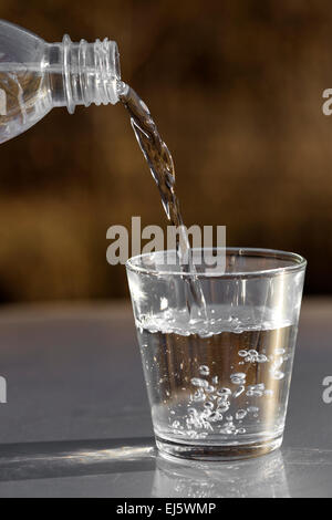 Gießt Wasser aus der Flasche ins Glas auf Natur Hintergrund Stockfoto