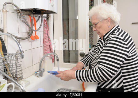 Ältere Frau wäscht Gerichte in ihrer Küche Stockfoto