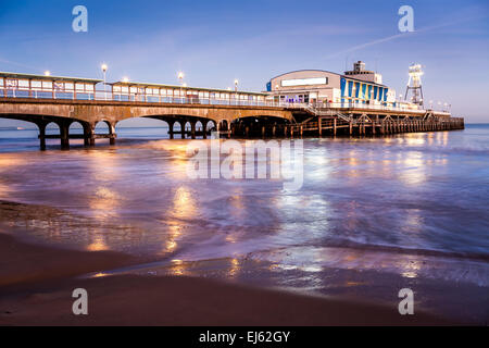 Die Lichter von Bournemouth Pier in der Nacht spiegelt sich in dem nassen Sand am Strand. Dorset England UK Europa. Stockfoto