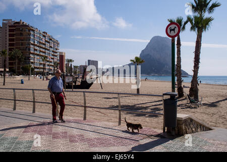 Ein Mann geht seinen Hund entlang der Strandpromenade im spanischen Urlaubsort Calpe an der Costa Blanca. Stockfoto