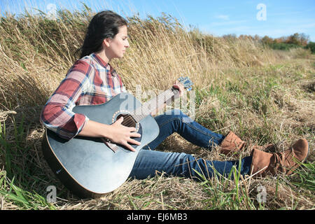 Hippie-Mädchen vom Lande mit Gitarre an Weizen Feld Trink schwarz ca Stockfoto