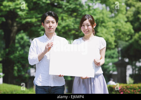 Junge japanische paar halten lächelnd weiße Board in einem park Stockfoto