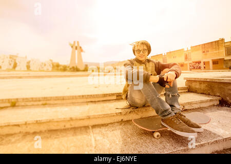 junger Rasta Mann im Freien sitzen auf seinen Skate mit einem warmen Filter angewendet Stockfoto