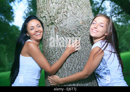 zwei glückliche Womans umarmt einen Baum im Vordergrund Stockfoto