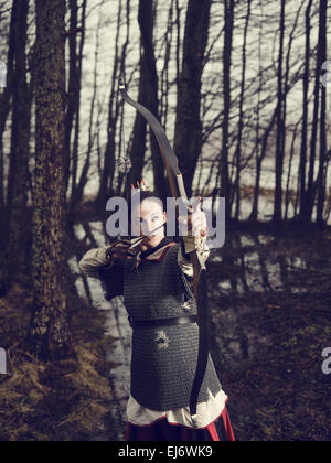 Mittelalterlicher Bogenschütze Frau, sie trägt ein Kettenhemd und Verwendung einen Bogen und Pfeil, düsteren Wald, Crossen Bild. Stockfoto