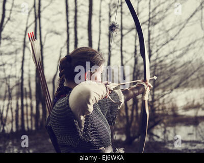 Mittelalterlicher Bogenschütze Frau, sie trägt ein Kettenhemd und Verwendung einen Bogen und Pfeil, düsteren Wald, Crossen Bild. Stockfoto