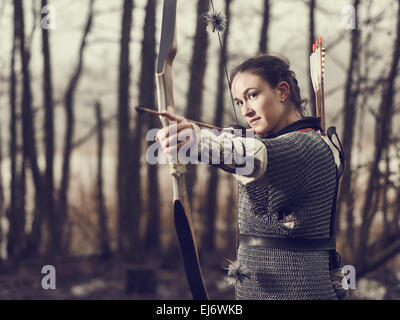 Mittelalterlicher Bogenschütze Frau, sie trägt ein Kettenhemd und Verwendung einen Bogen und Pfeil, düsteren Wald, Crossen Bild. Stockfoto