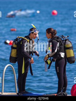 Zwei Taucher, wahrscheinlich ein Tauchlehrer und ein Schüler, bereiten sich darauf vor, im blauen Wasser der Saint Pauls Bay zu tauchen - St. Pauls Bay, San Pawl il-Bahar, Malta. Stockfoto