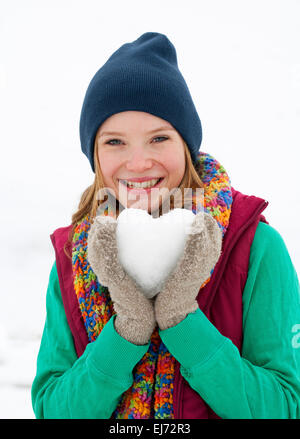 Junge Frau, 22 Jahre alt, hält ein Herz aus Schnee gemacht Stockfoto