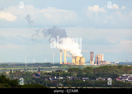 Blick von einer Halde über ländliche Landschaft zu einem fernen dampfenden Kohle befeuerten Kraftwerk umgeben von Windkraftanlagen. Stockfoto