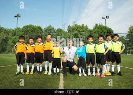 Der Fußball-Trainer und die Jungs stehen in einer Reihe in dem Fußballplatz Stockfoto