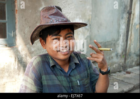 Glücklich lächelnd Porträt des birmanischen Jüngling Holding Cheroot und trägt einen Hut auf den Straßen von Yangon Myanmar Burma Stockfoto