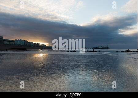 Sonnenaufgang über Brighton Strand, Strandpromenade und Mole, zwei entfernten Figuren in Silhouette, dramatische Wolken, Ebbe Stockfoto