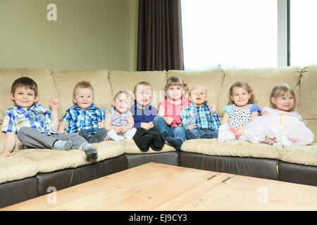acht kleine Kinder sitzen auf dem Sofa im Wohnzimmer. Stockfoto