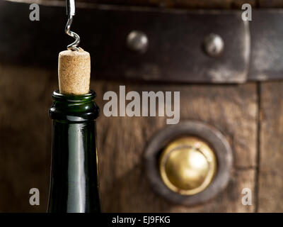Öffnen einer Weinflasche mit Korkenzieher mit Holzfass auf dem Hintergrund. Stockfoto