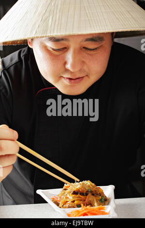 Mann in konische asiatischen Hut Essen Stockfoto