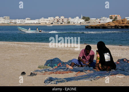 Fischer und Frau ausbessern Netze am Strand, Sur, Oman Stockfoto