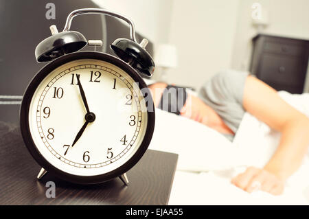 Nahaufnahme eines Weckers auf 6,55 morgens auf dem Nachttisch und ein junger kaukasischen Mann schlafend im Bett mit einem schwarzen Schlaf Stockfoto