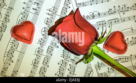 Rote Rose auf Partituren mit Schokoladenherzen rund um Stockfoto