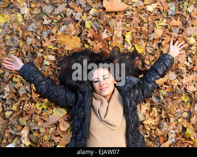 Frau auf dem Rücken liegend im Herbst Blätter Stockfoto