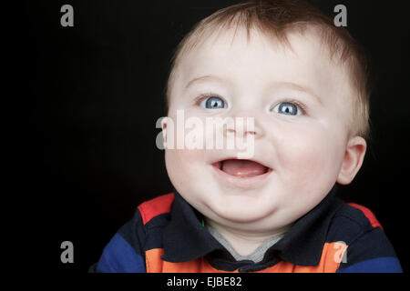 Eine junge, lächelnde Baby starrt die Kamera auf ein Bla isoliert Stockfoto