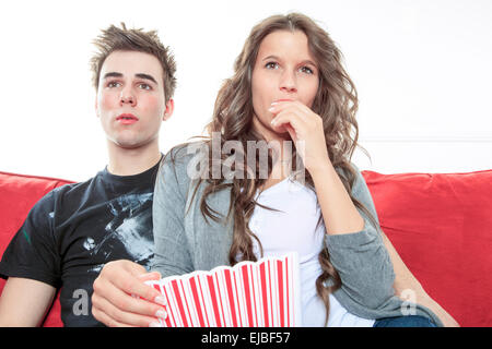 Porträt des jungen Paares sitzen zusammen auf dem Sofa zu Hause vor dem Fernseher, freudig lächelnd essen Popcorn genießen Sie eine Nacht in zusammen zu schließen. Home Lifestyle und Entertainment-Technologie. Stockfoto